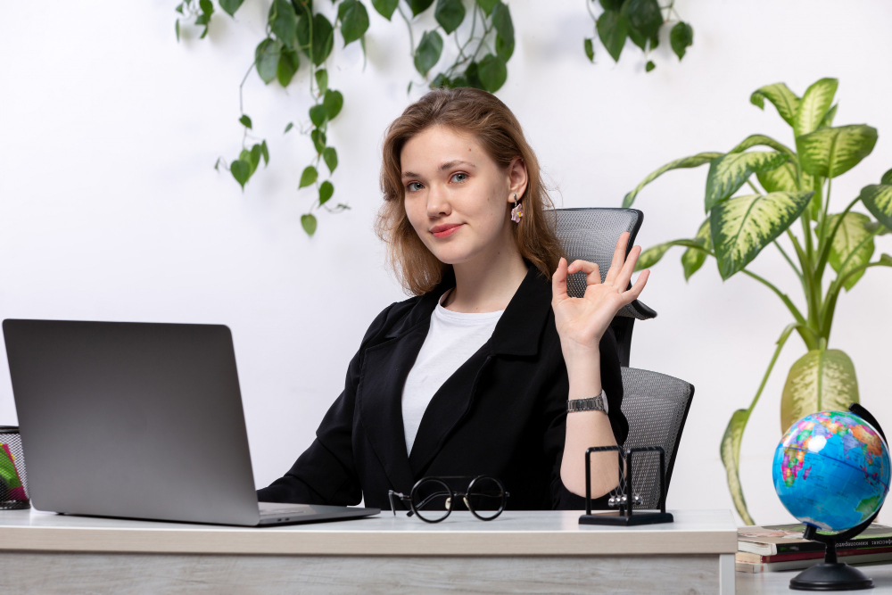 A woman in a business suit is sitting at her desk with a laptop, utilizing the power of virtual assistants for marketing.
